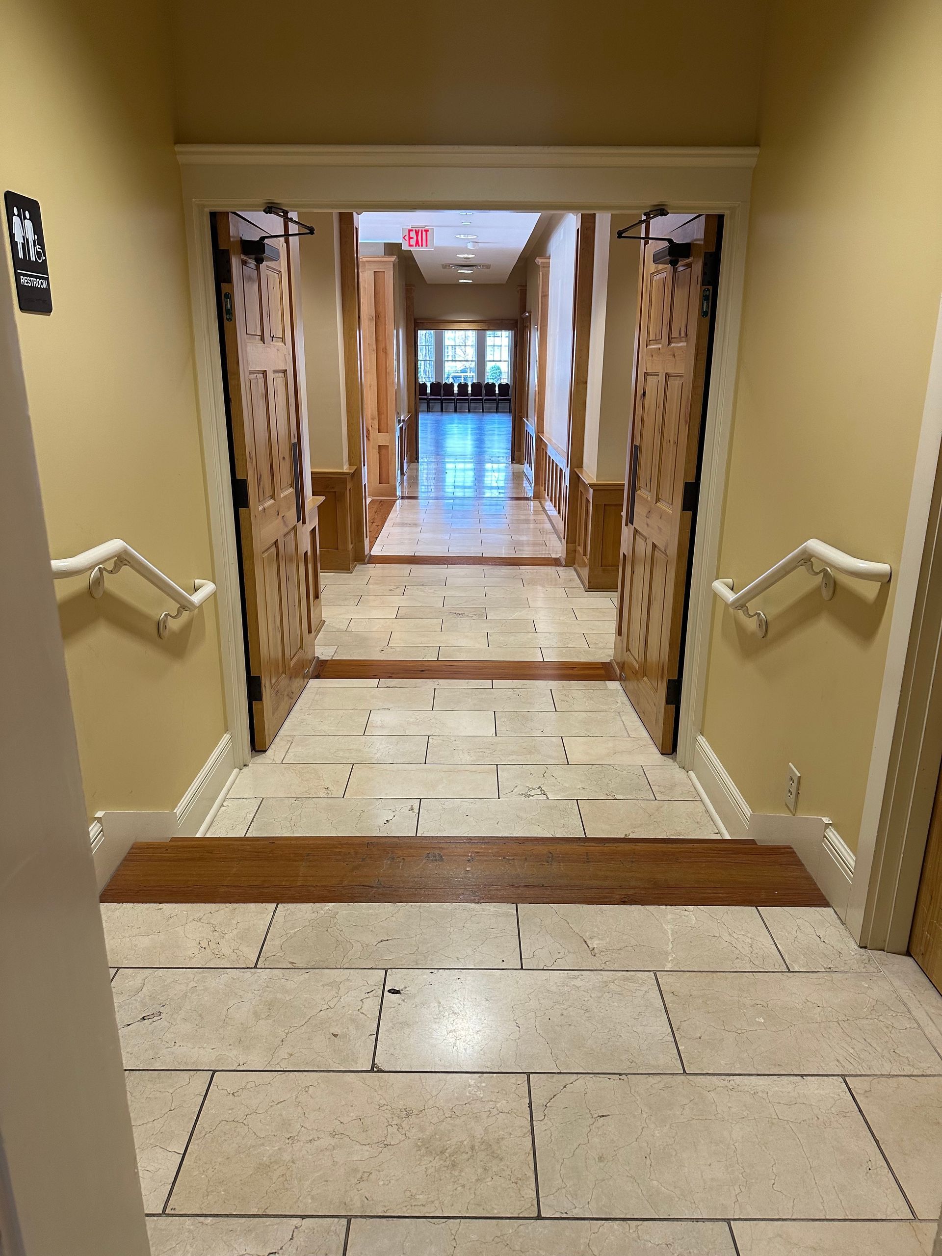 Interior stair corridor with beige tiled steps, wooden doors, and a hallway leading to glass doors in the distance