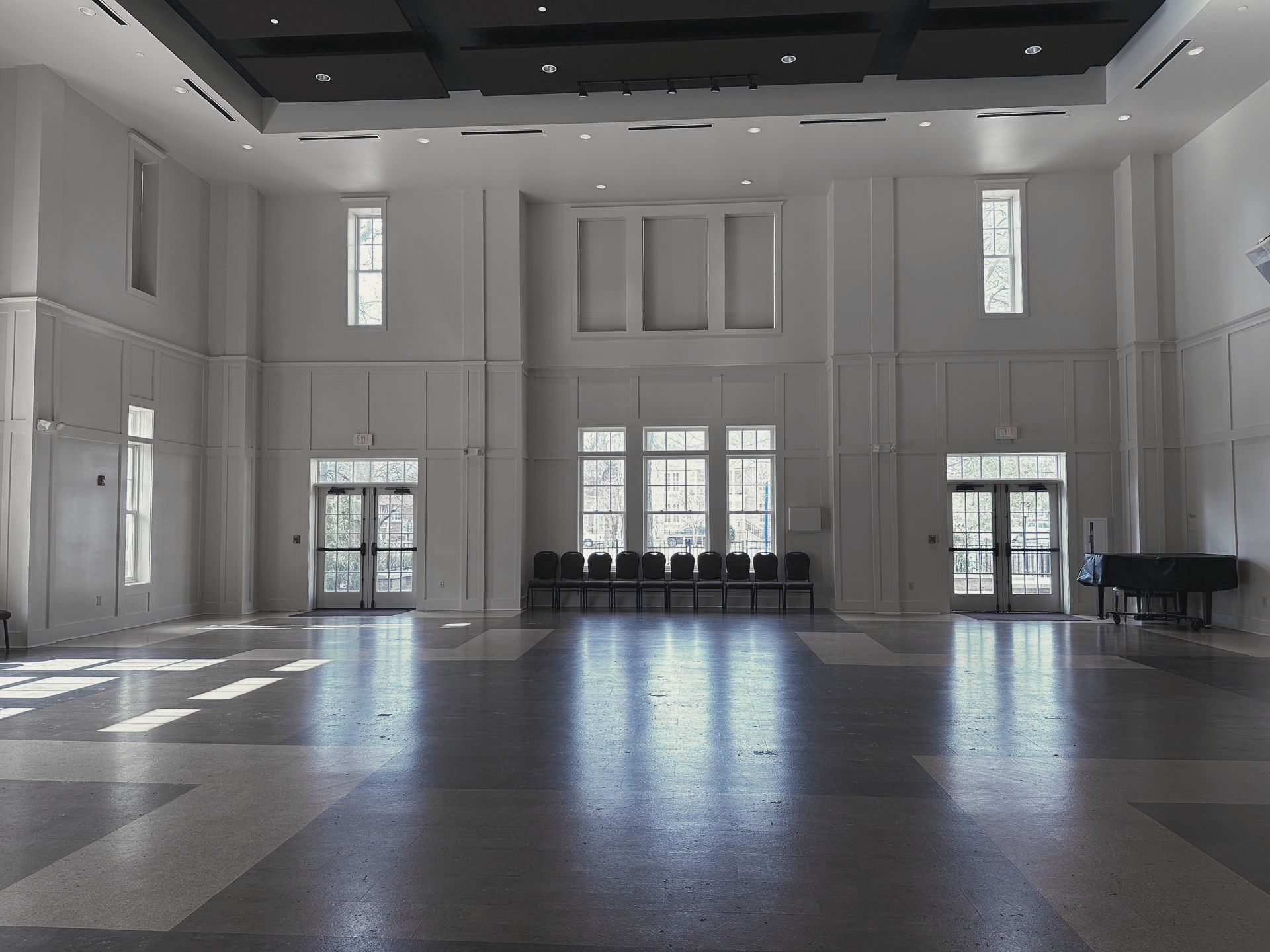 Empty modern lobby with tall windows, white walls, and a polished dark floor flooded with daylight