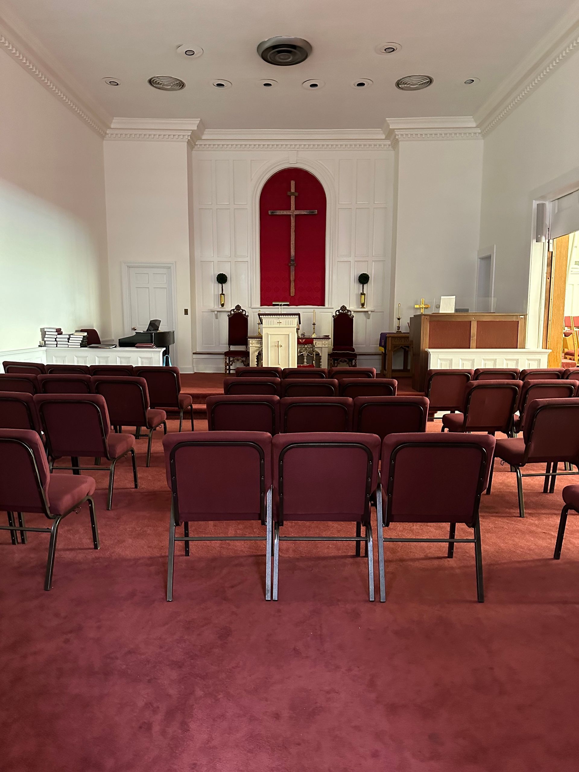 Empty church interior with rows of red chairs facing an altar and red cross backdrop