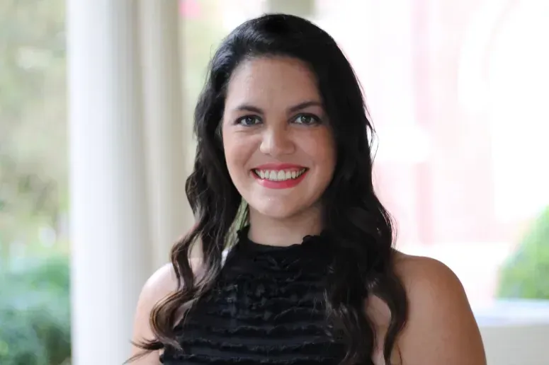 Smiling woman with long dark hair in a black lace top against a softly lit background