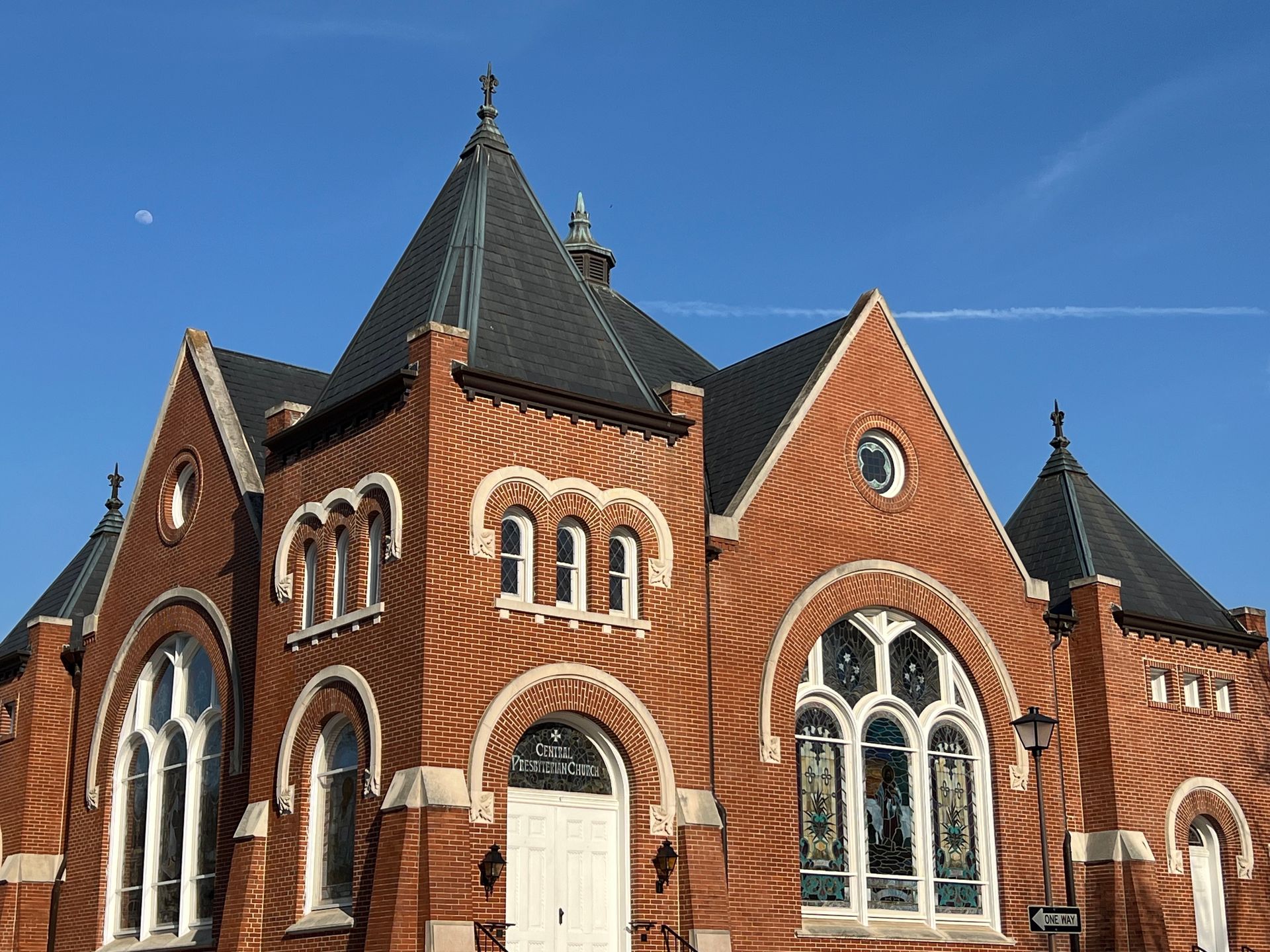 Red brick church with arched windows and dark roof against a blue sky