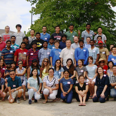 Large group of people posing outdoors in front of trees, seated and standing in rows