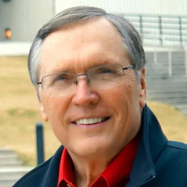 Smiling man in glasses wearing a red shirt and dark jacket outdoors