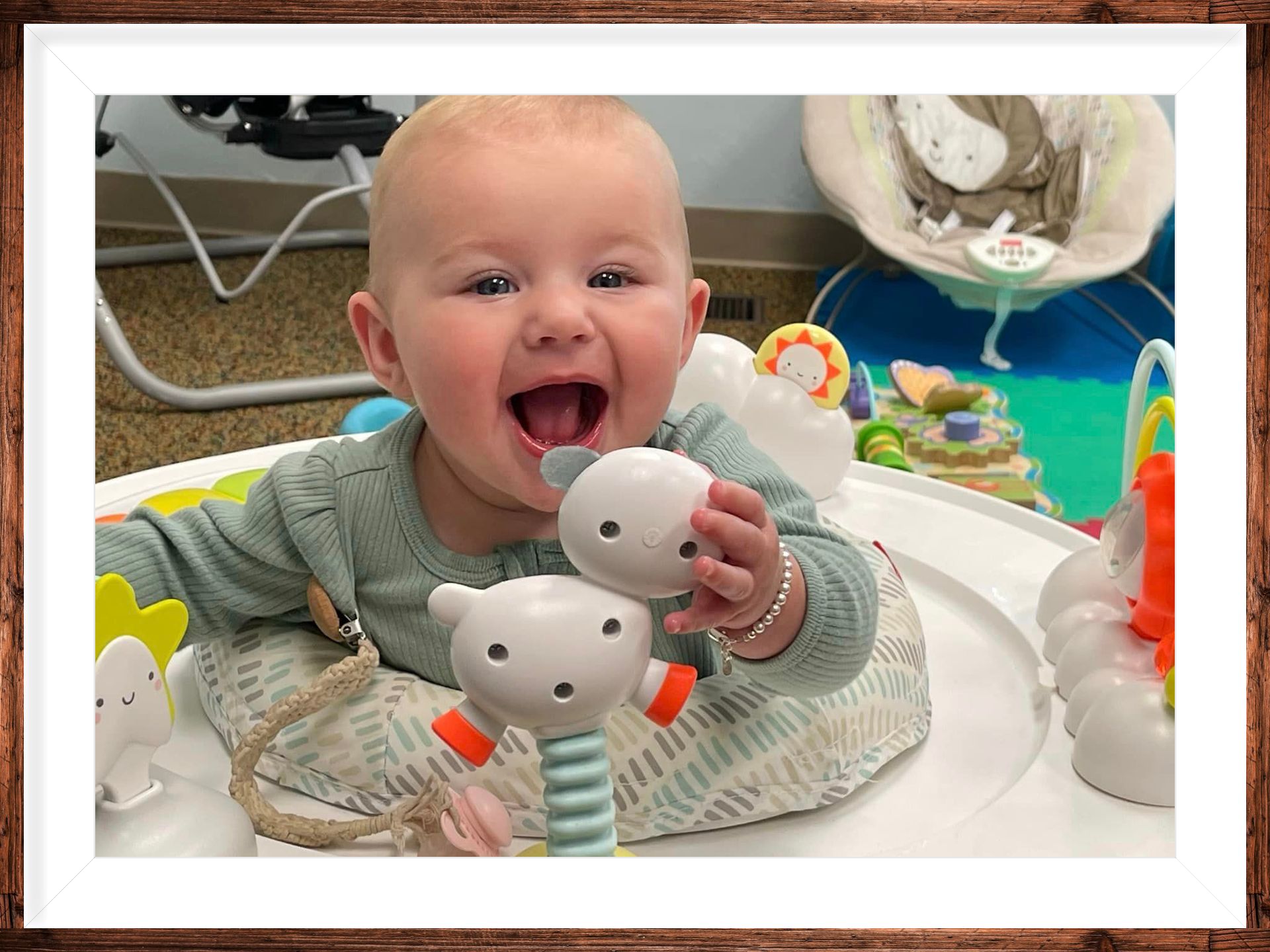 Smiling baby in a high chair reaching for a gray toy at a colorful play area