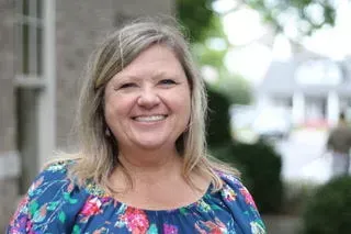 Smiling person in a blue floral blouse standing outdoors with a blurred background