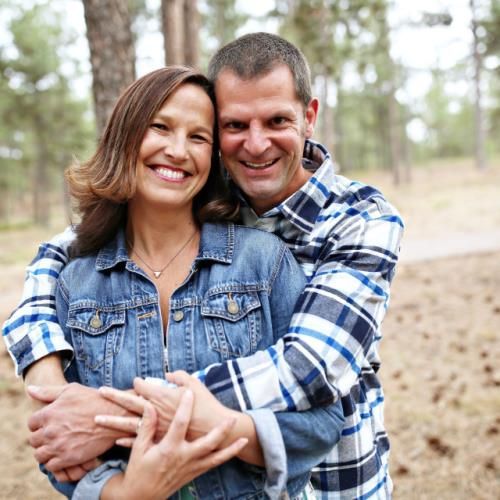 Smiling couple hugging outdoors in a forest, wearing denim and plaid shirts