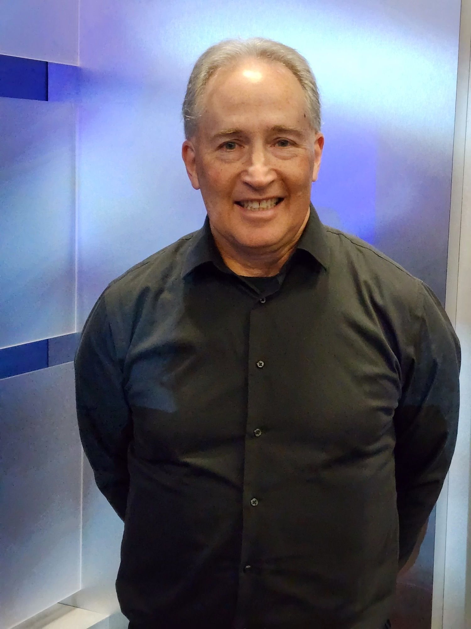 Smiling man in a black shirt standing against a blue-lit wall