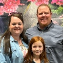 Three people posing in front of pink flowers, smiling at the camera.