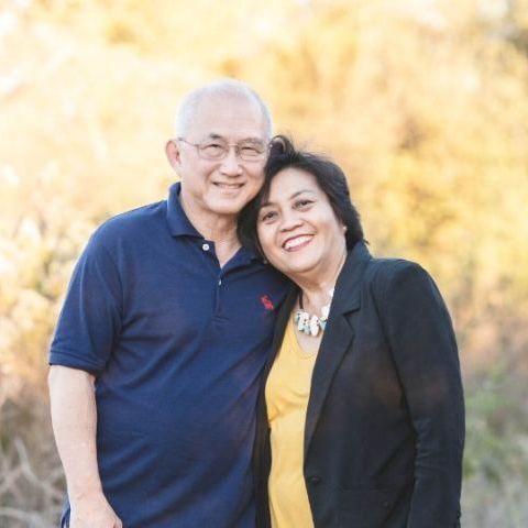 Smiling couple in casual clothes standing close together outdoors against a warm, blurred background