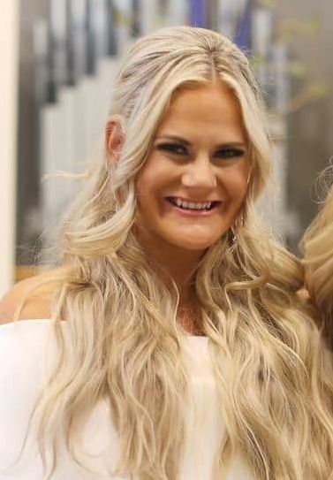 Smiling blonde woman in a white top with long wavy hair, standing indoors