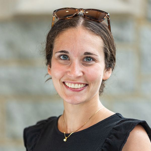 Smiling woman with sunglasses on head, wearing a black top, against a softly blurred background