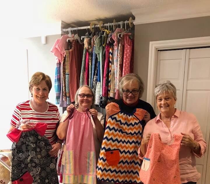 Four people holding colorful garments in front of a wall display of hanging clothes