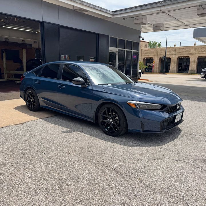 Blue sedan parked outside a garage, shown in three-quarter front view on a sunny day