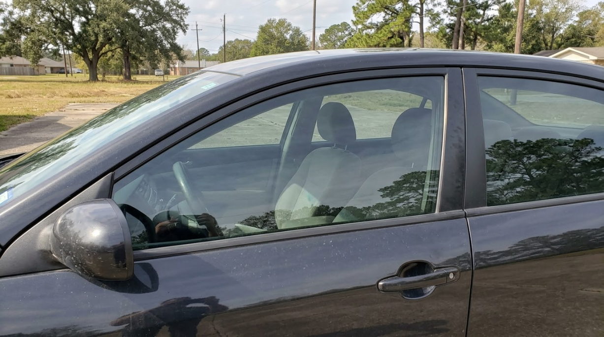 Black car parked roadside with trees and grass in the background