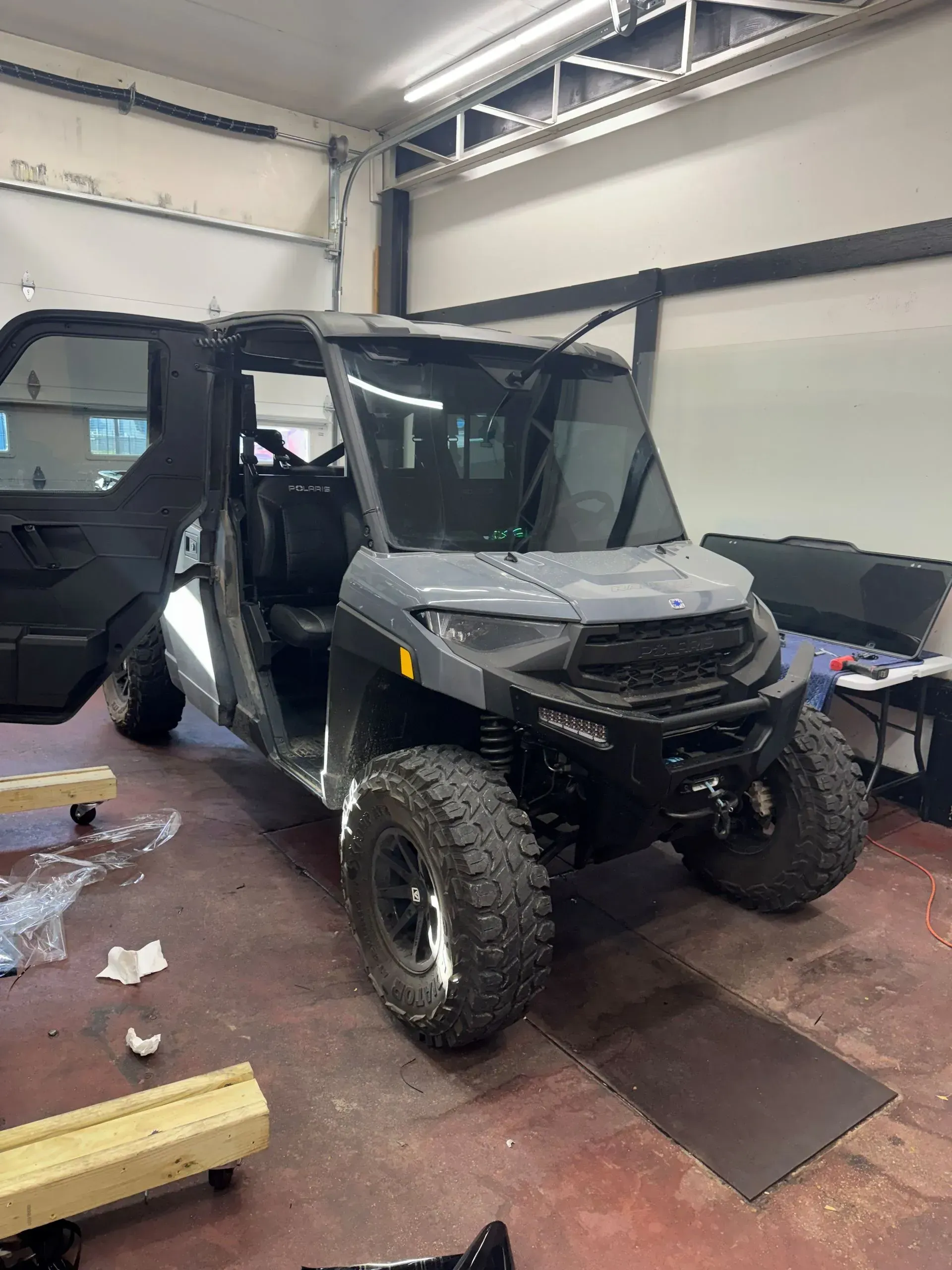 Black off-road utility vehicle inside a garage, with doors open and front windshield folded up