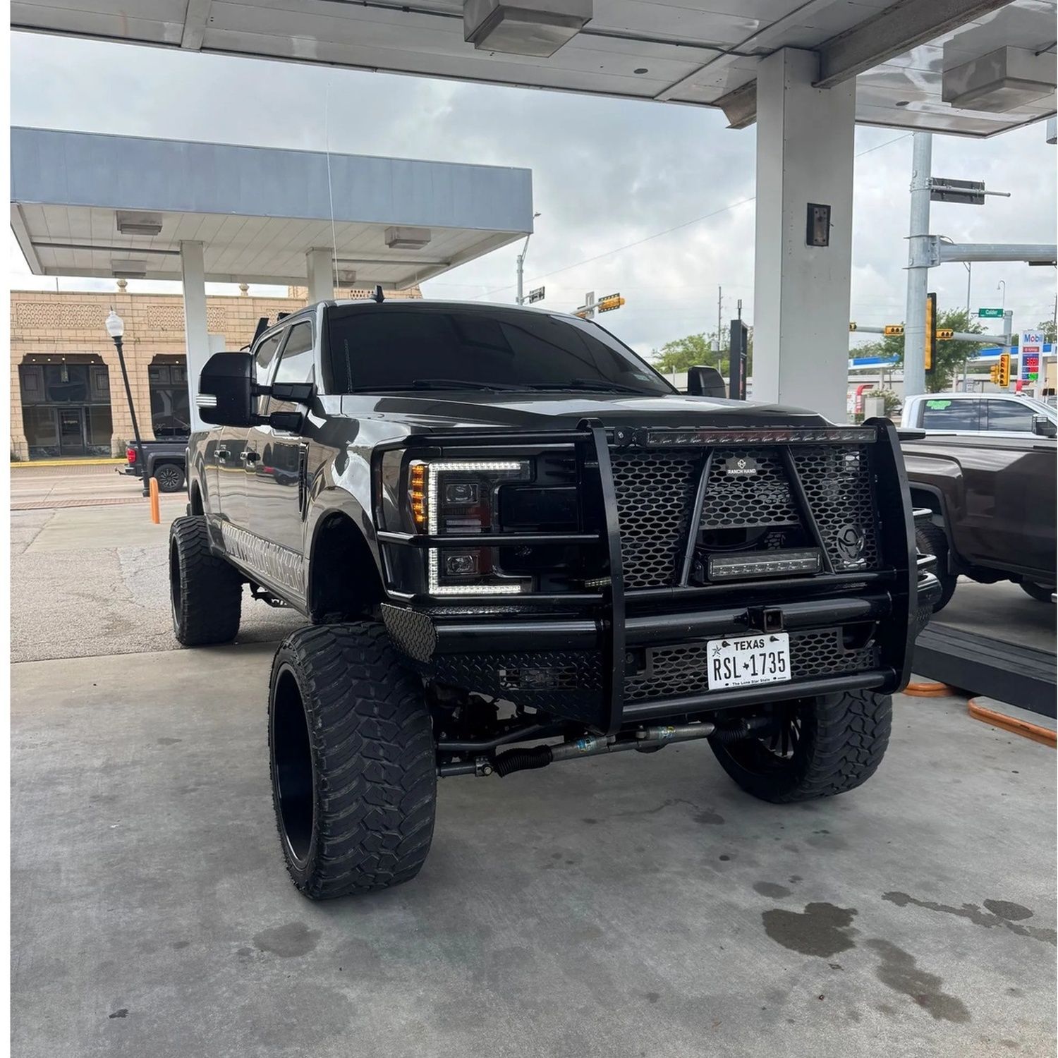 Black lifted pickup truck at a gas station, front view, with a heavy-duty grille guard.