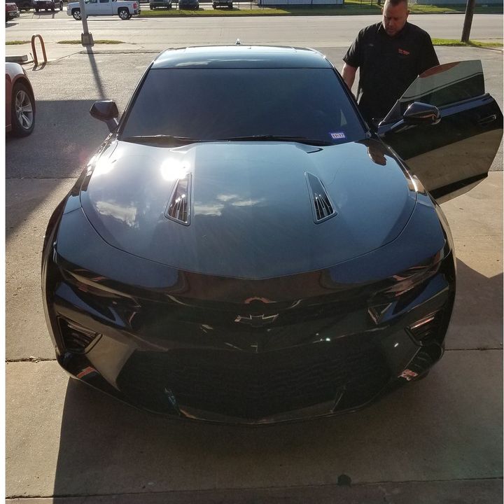 Black sports car parked on a driveway with a man standing by the open passenger door