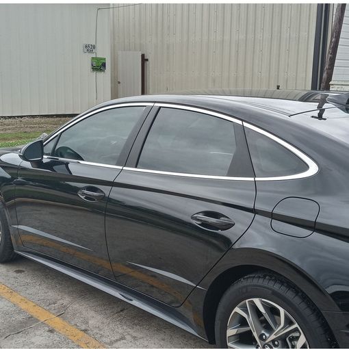 Black sedan parked beside a beige building, shown from the side.