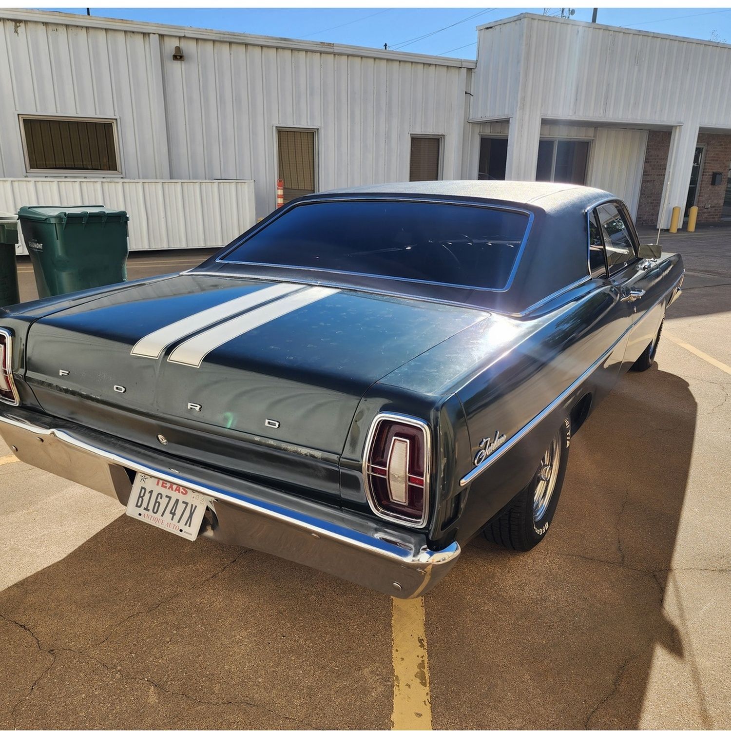 Classic dark green vintage car with white racing stripes parked outside a metal building.