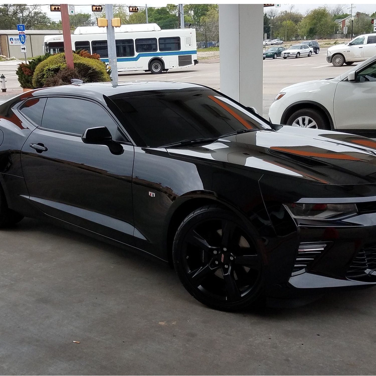 Black sports car parked under a canopy at a dealership, with tinted windows and black rims.