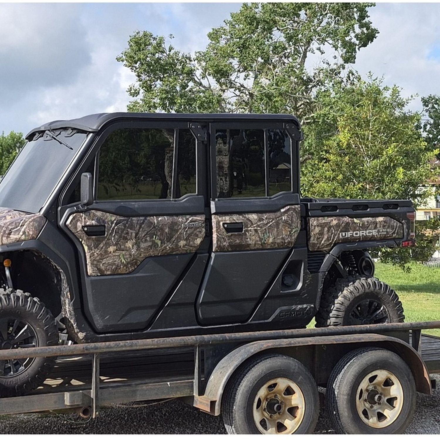 Camouflaged side-by-side utility vehicle on a trailer outdoors with trees in the background