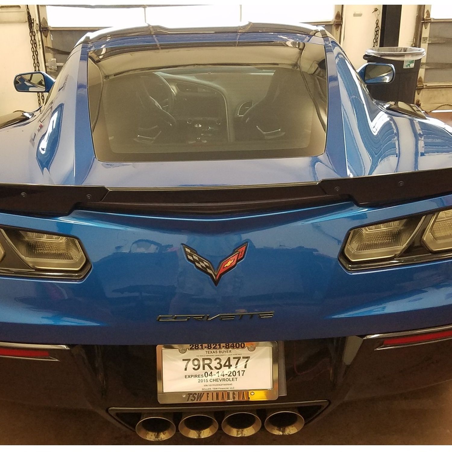 Rear view of a blue Chevrolet Corvette with a black spoiler in a garage, license plate visible