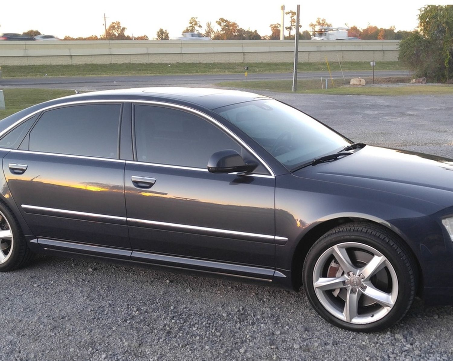Dark gray sedan parked on gravel beside a road at sunset
