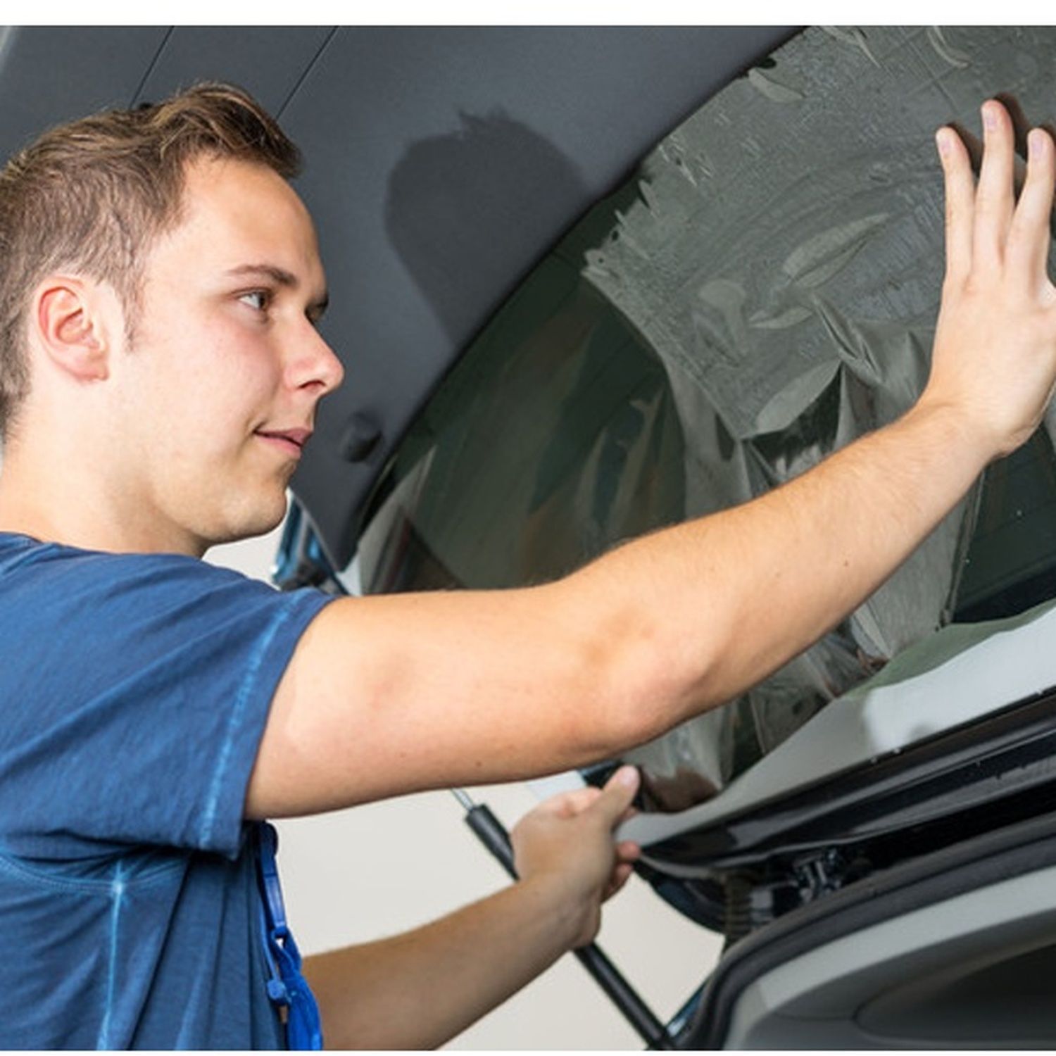 Man cleaning a car windshield with a cloth in a garage