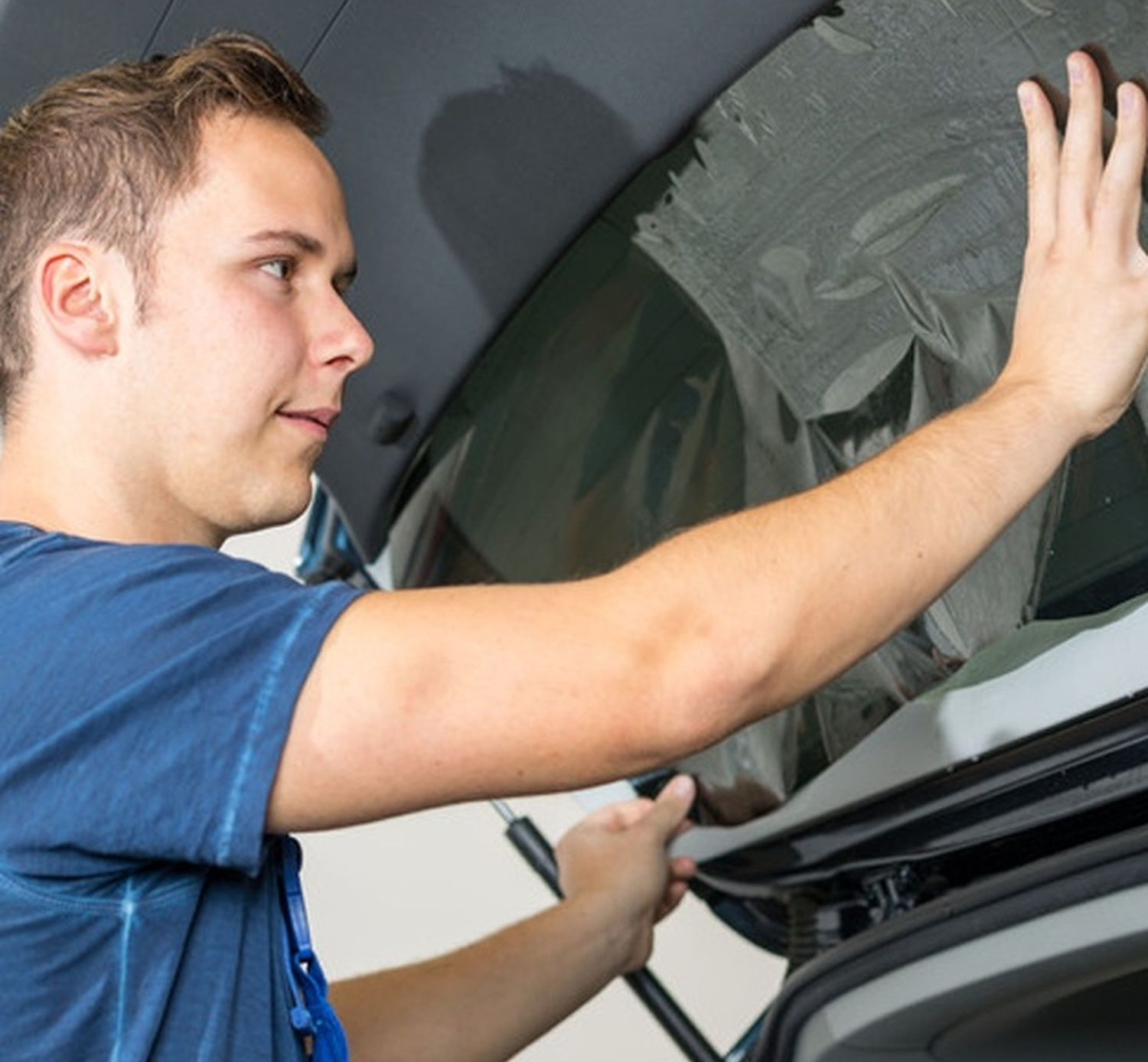 Man cleaning a car windshield with a cloth inside a garage