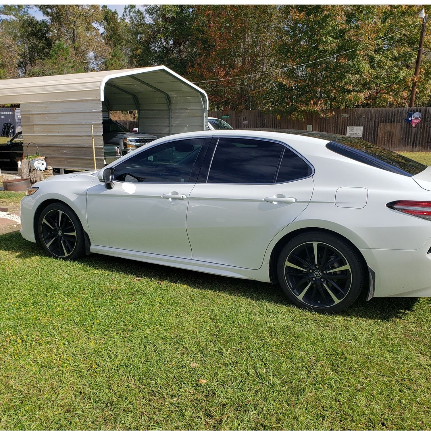 Silver sedan parked on grass beside a metal carport in a yard
