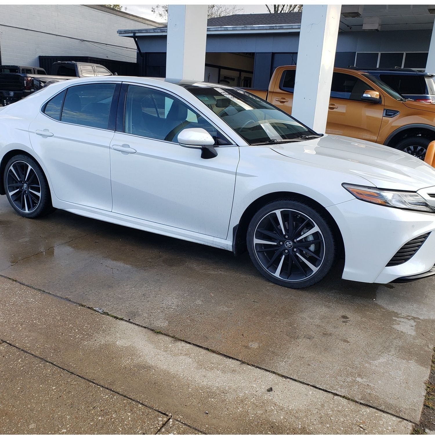White sedan parked at a wet dealership lot, side view under a covered area