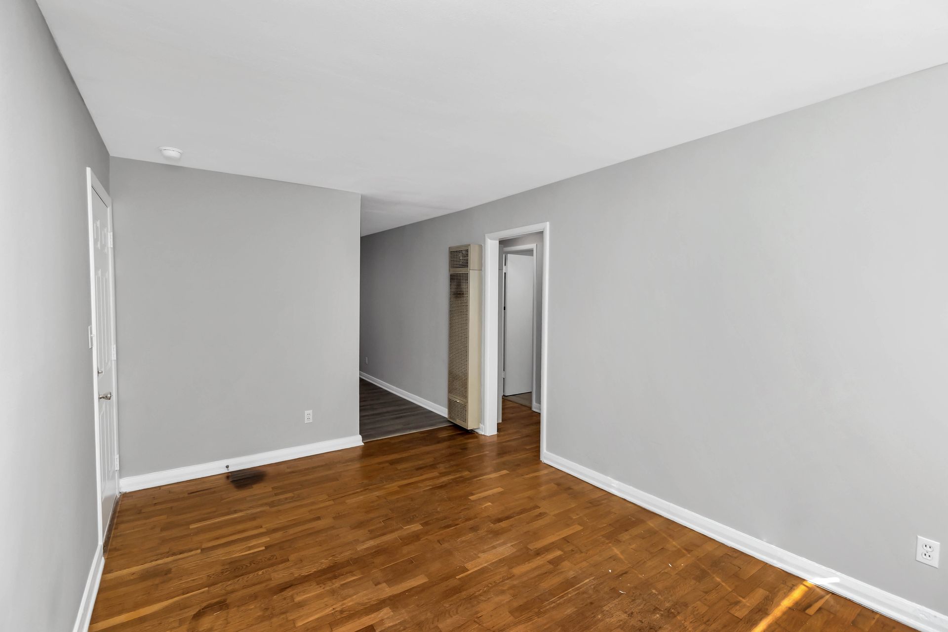 An empty living room with hardwood floors and gray walls.