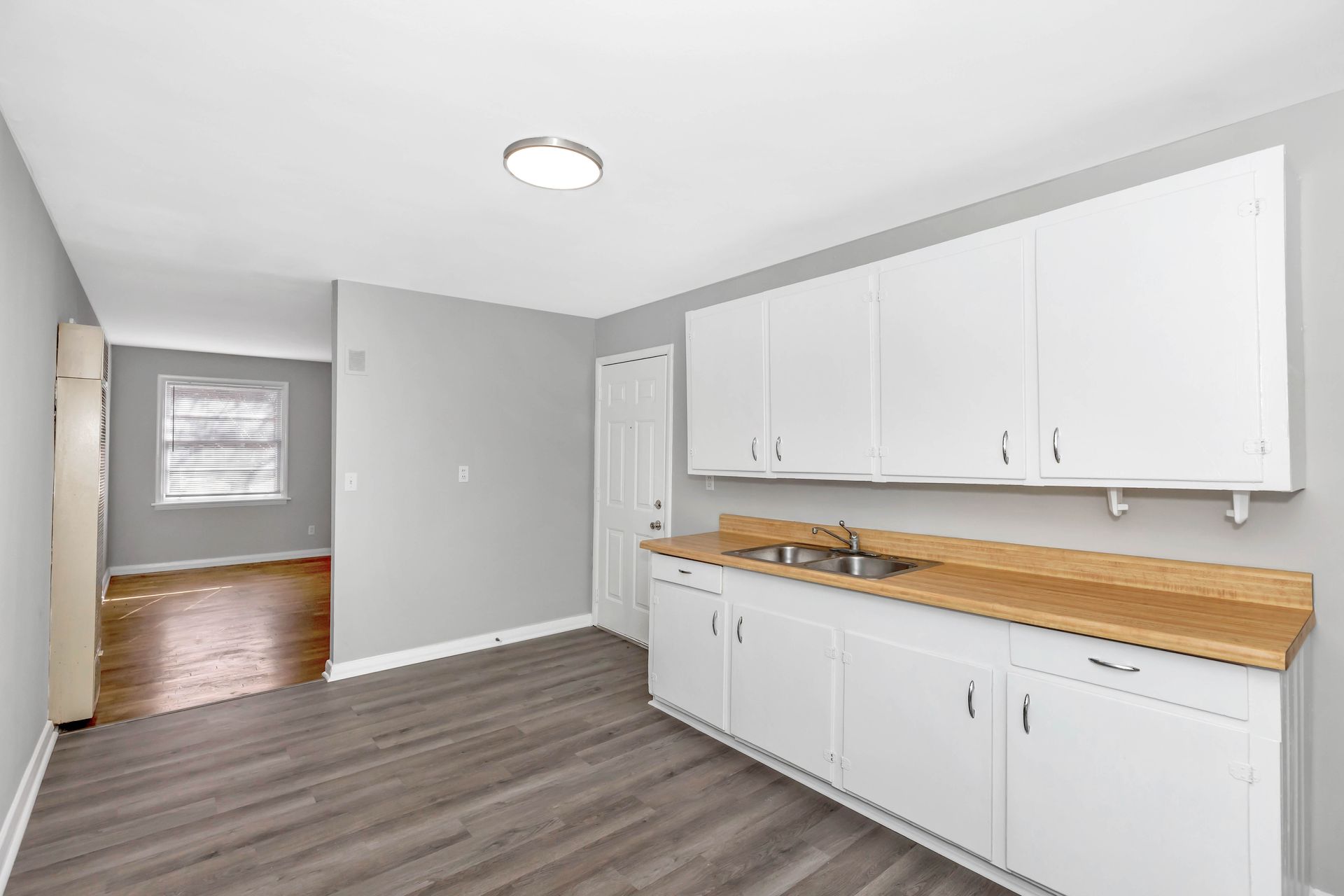 An empty kitchen with white cabinets and wooden counter tops.