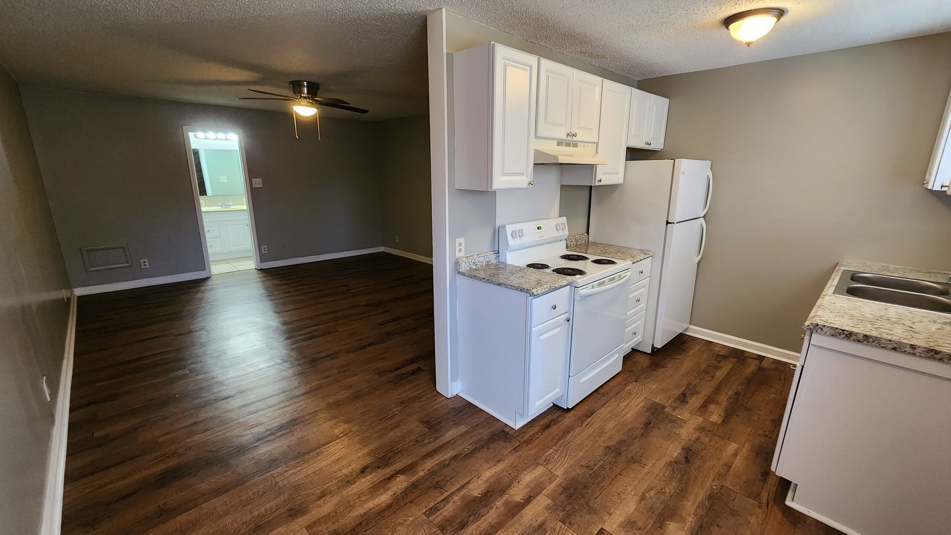 A kitchen with a stove , refrigerator , cabinets and hardwood floors.
