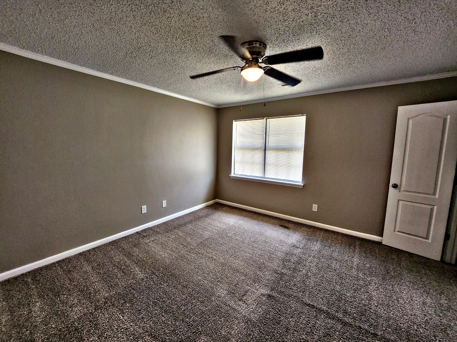 An empty bedroom with a ceiling fan and a window.