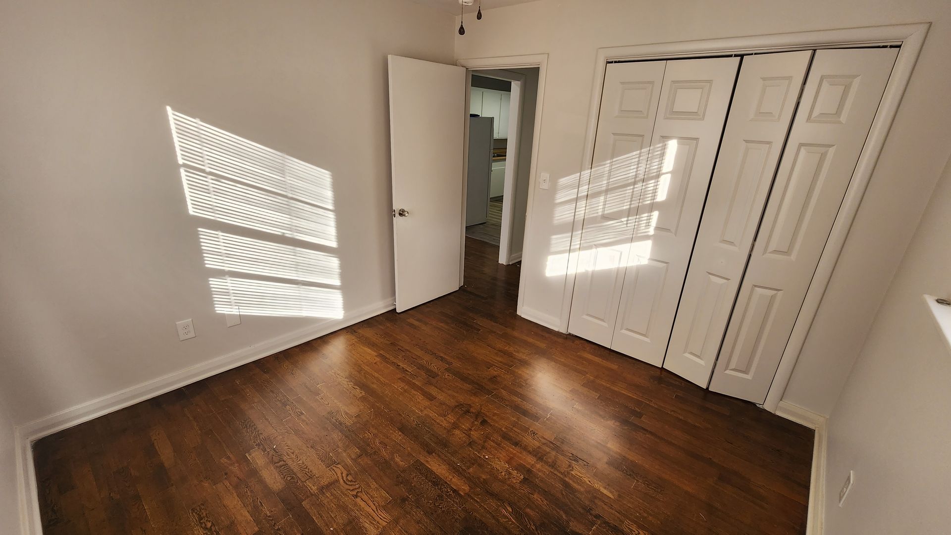 An empty bedroom with hardwood floors and white walls.