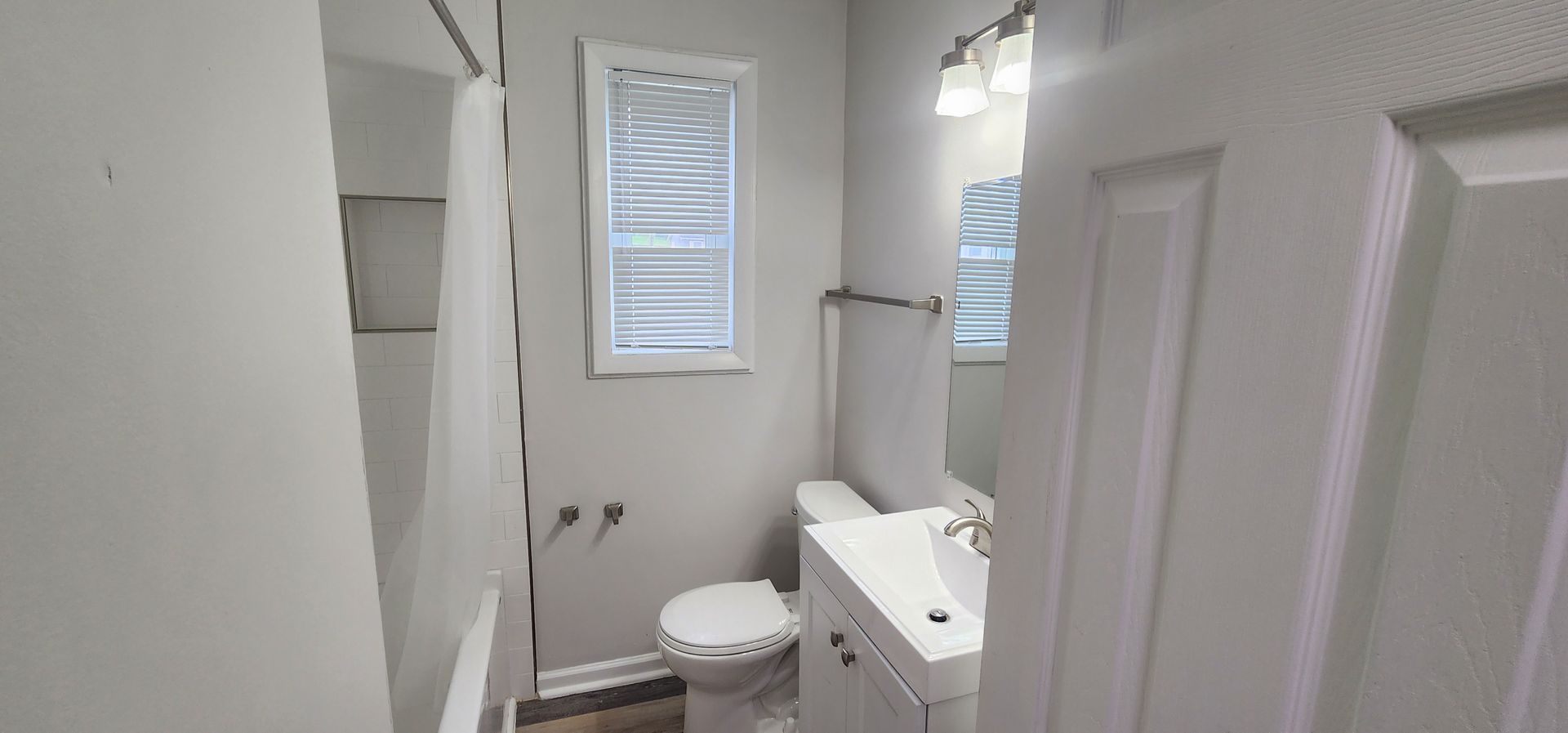A bathroom with a toilet , sink , mirror and window.