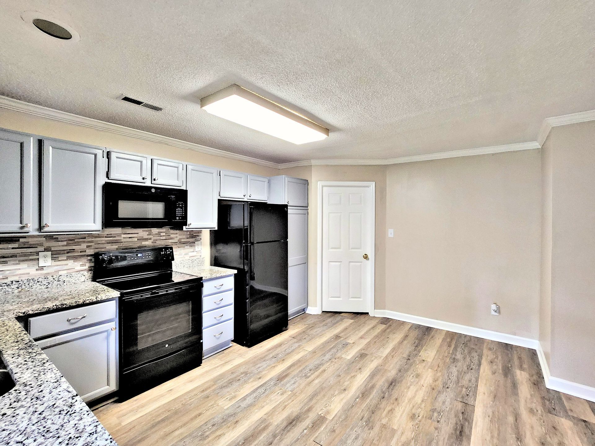 A kitchen with white cabinets , black appliances , a refrigerator and a microwave.