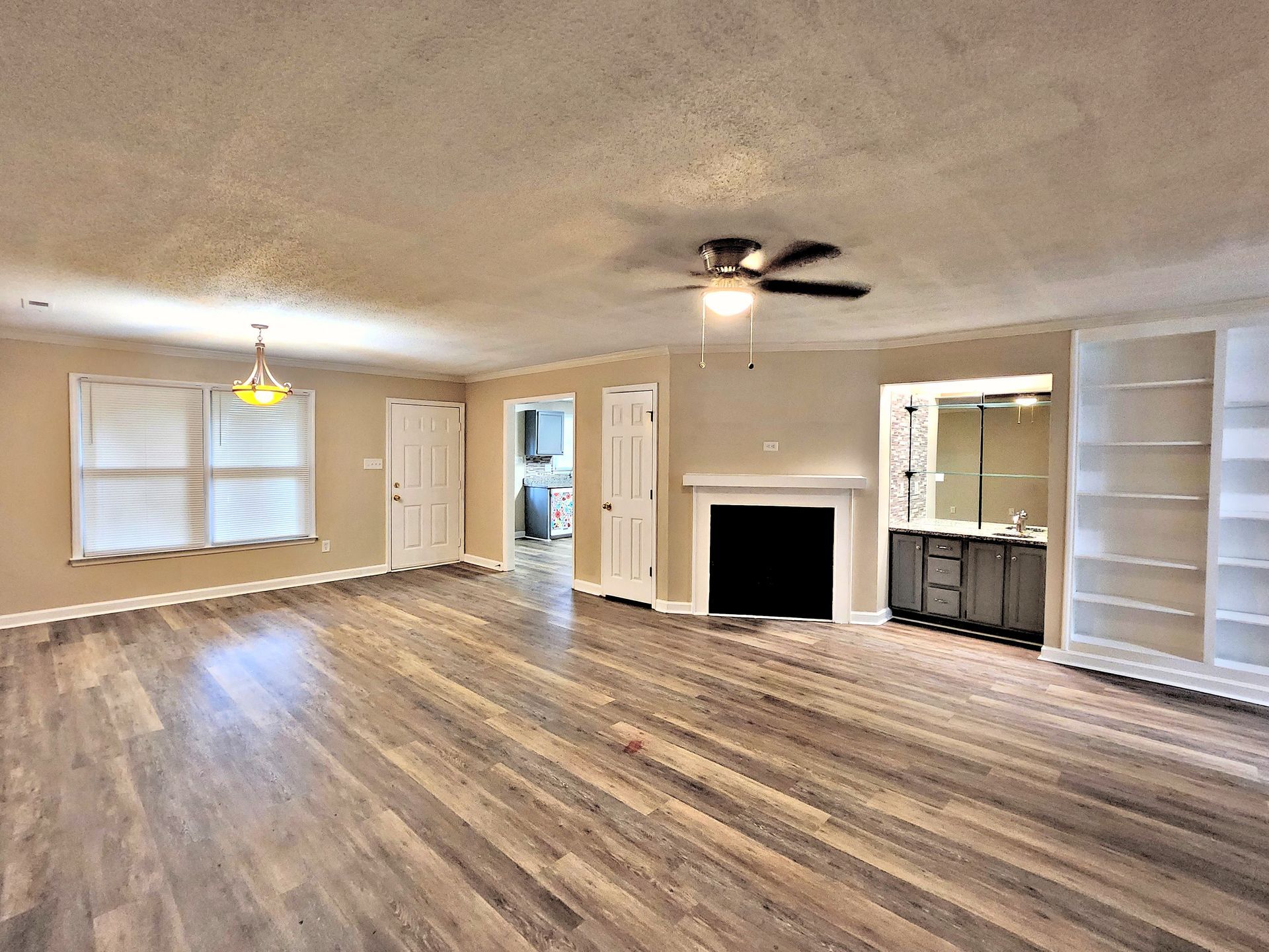An empty living room with hardwood floors , a fireplace and a ceiling fan.