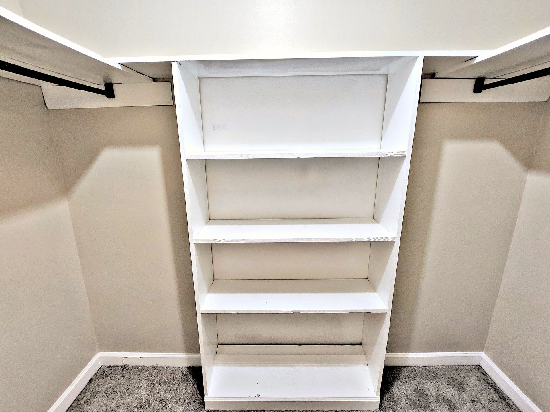 A walk in closet with a white shelf and a gray carpet.