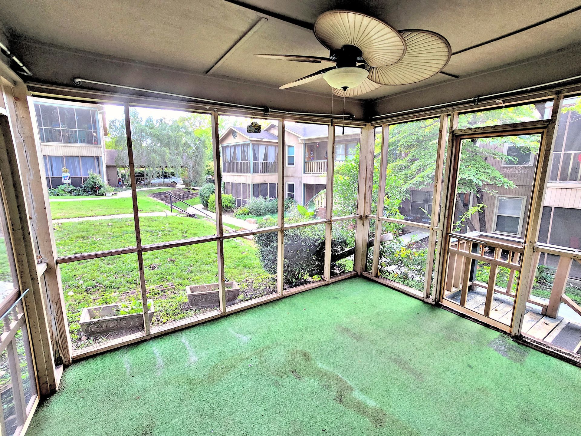 An empty screened in porch with a ceiling fan.