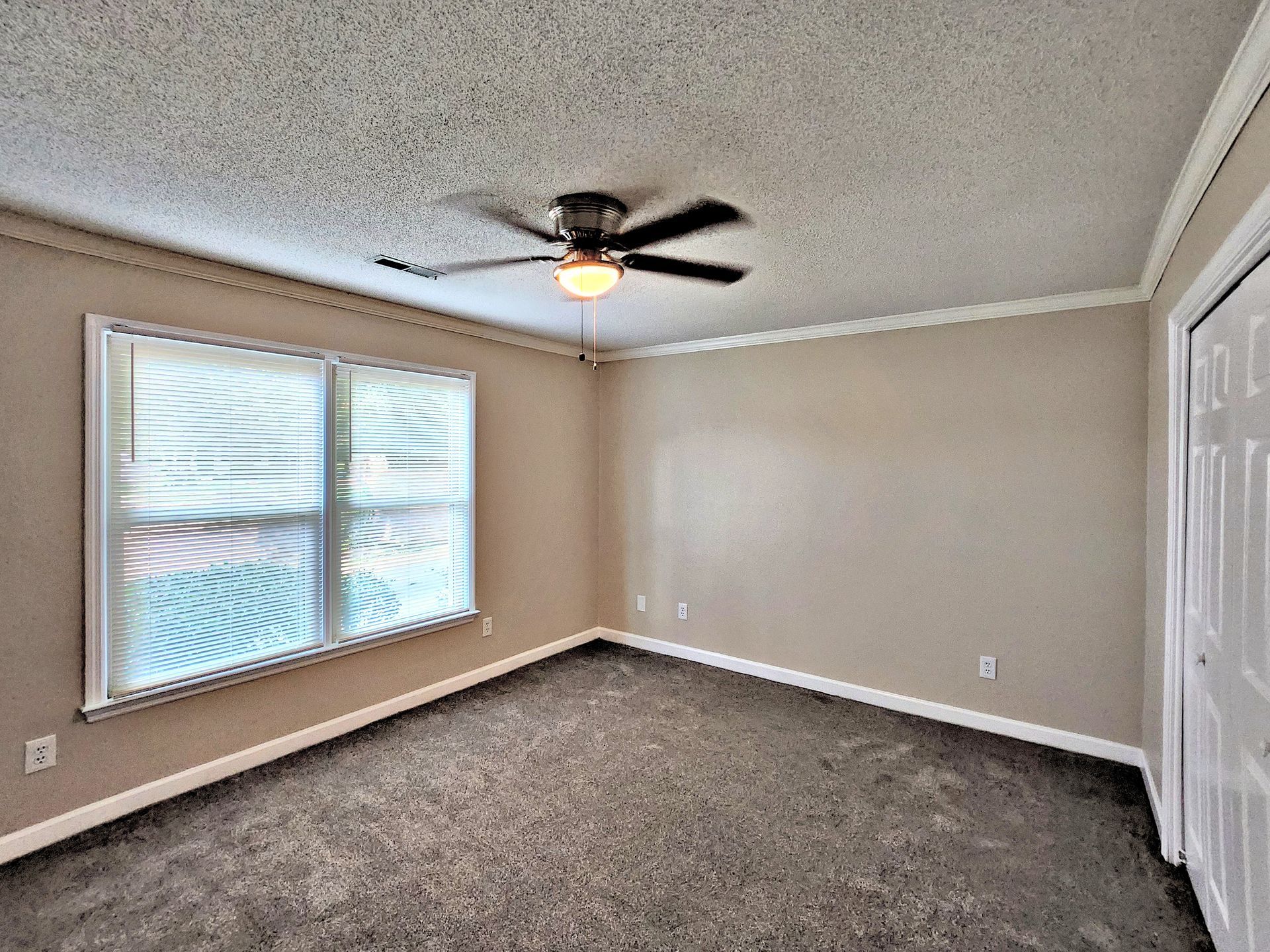 An empty bedroom with a ceiling fan and two windows.