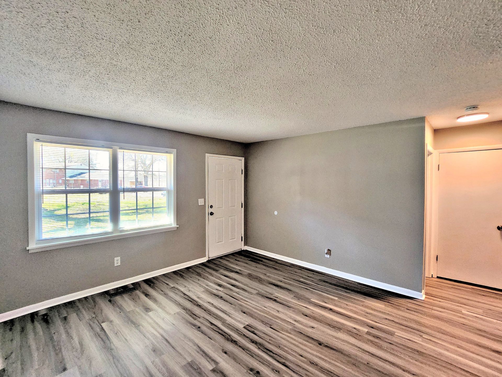 An empty living room with hardwood floors and a large window.