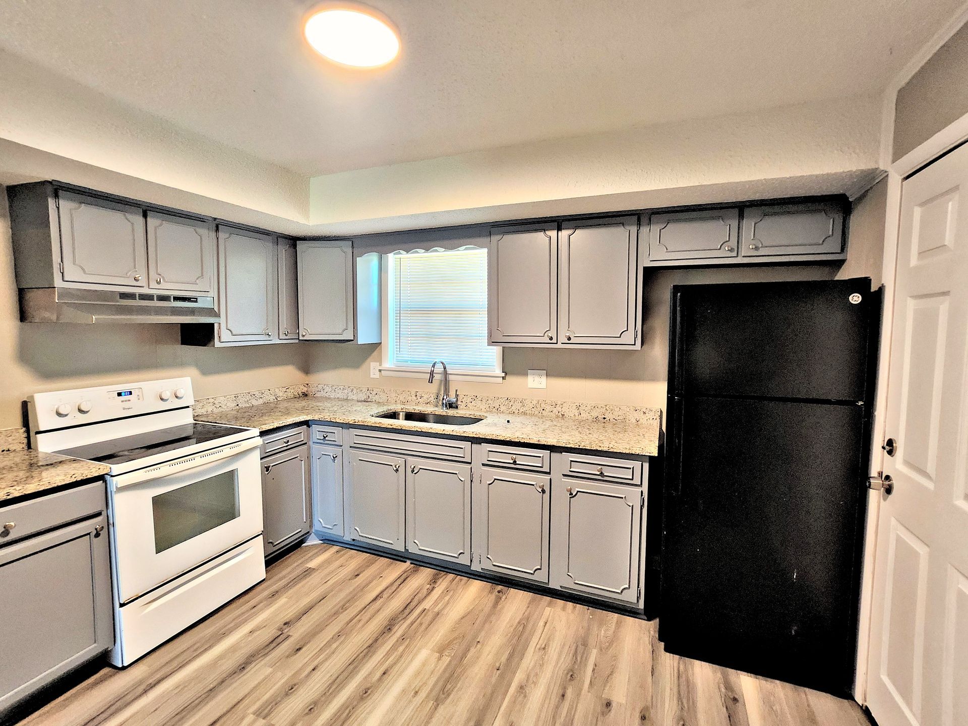 A kitchen with white cabinets , a black refrigerator , a stove , and a sink.