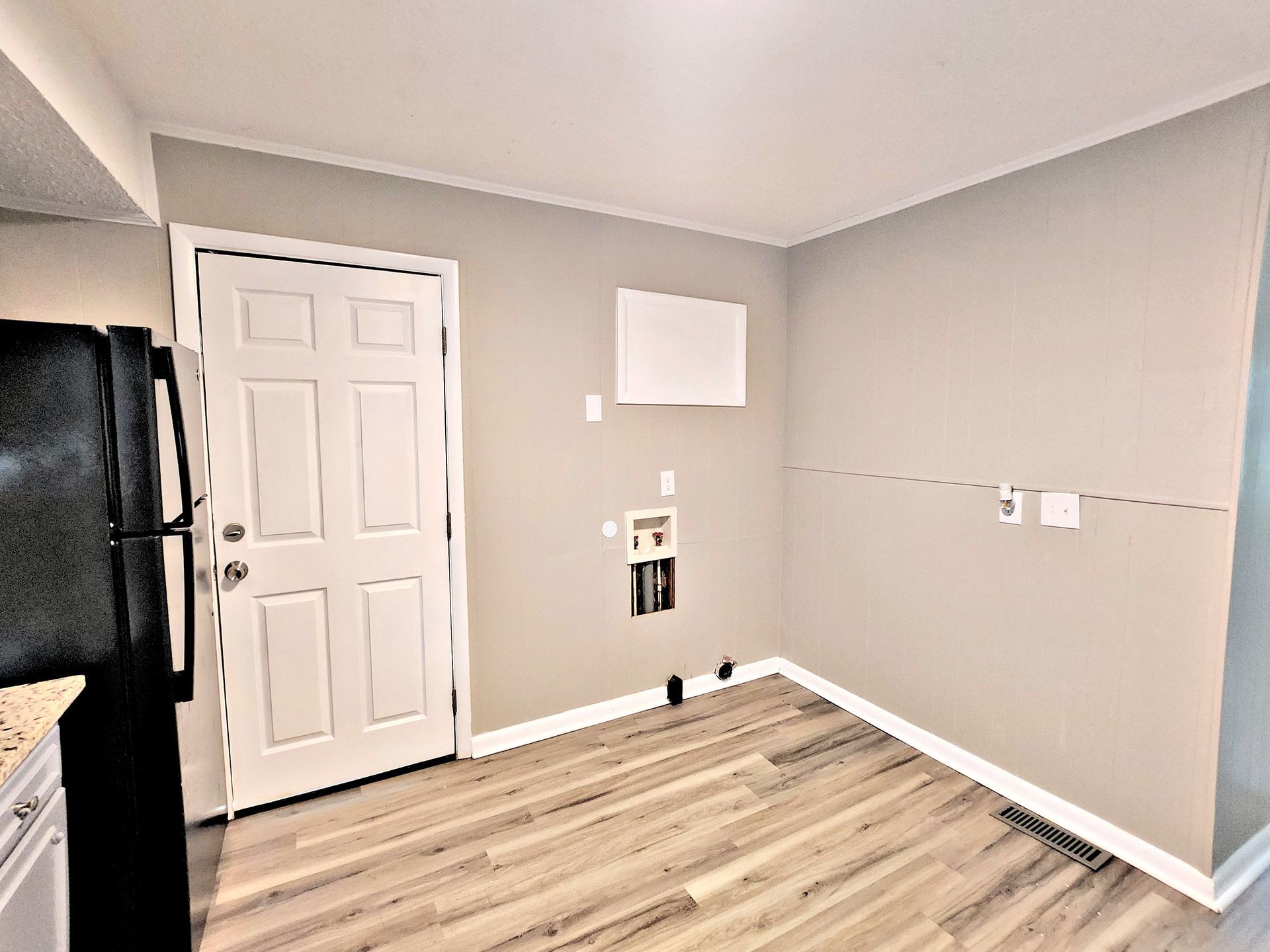 A kitchen with hardwood floors , a refrigerator , and a door.