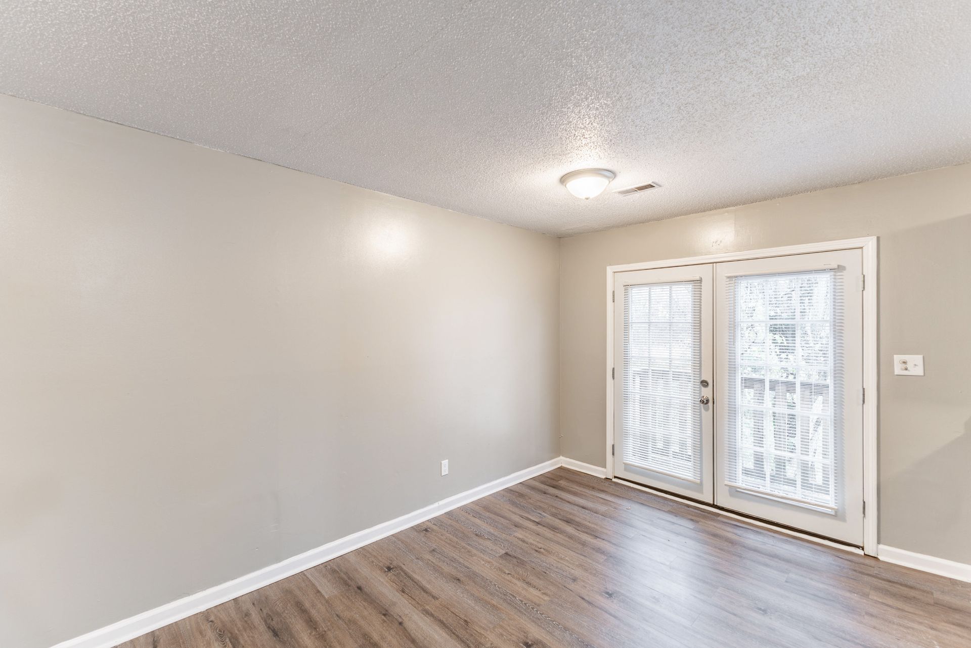 An empty living room with hardwood floors and sliding glass doors.