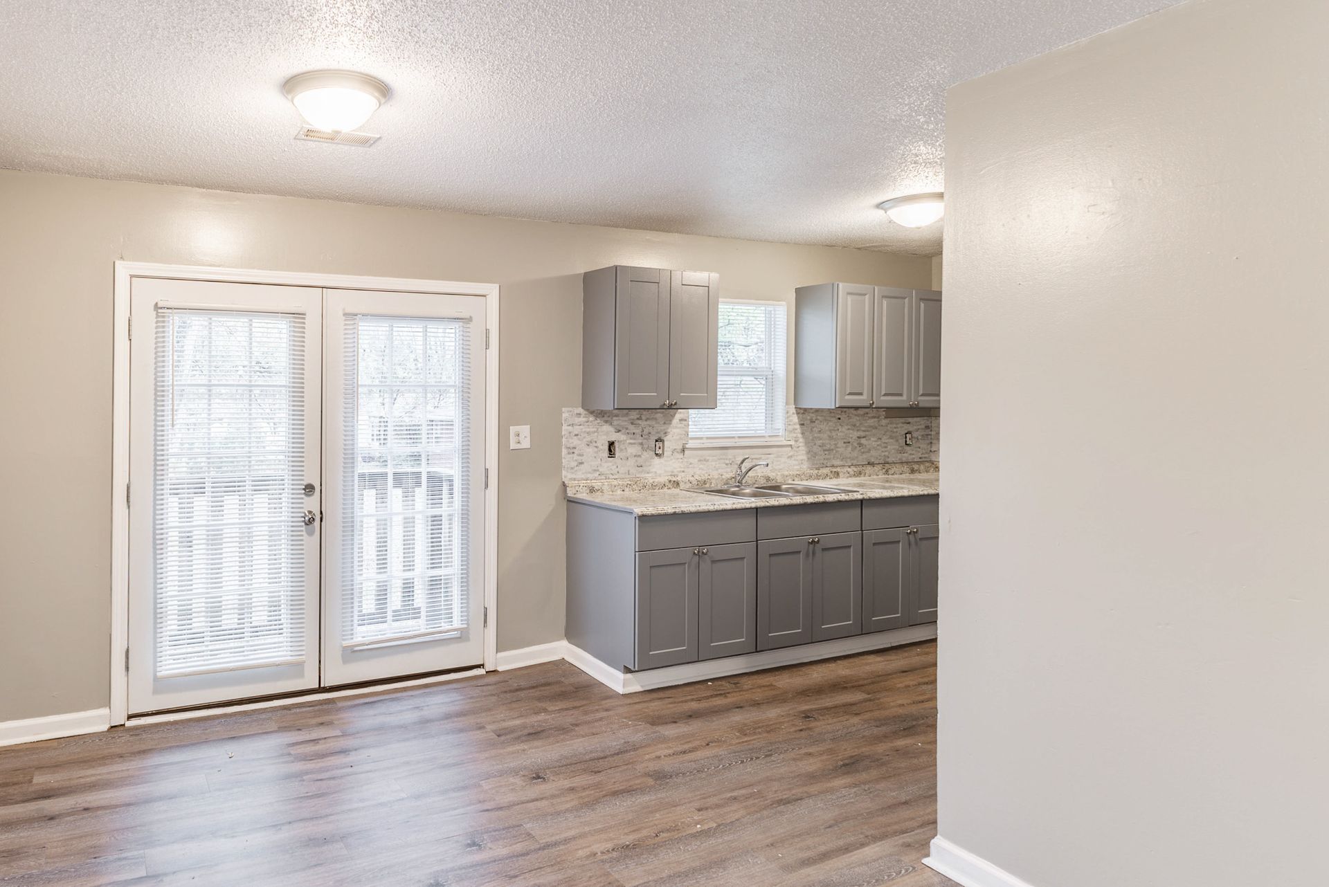An empty kitchen with gray cabinets and sliding glass doors.