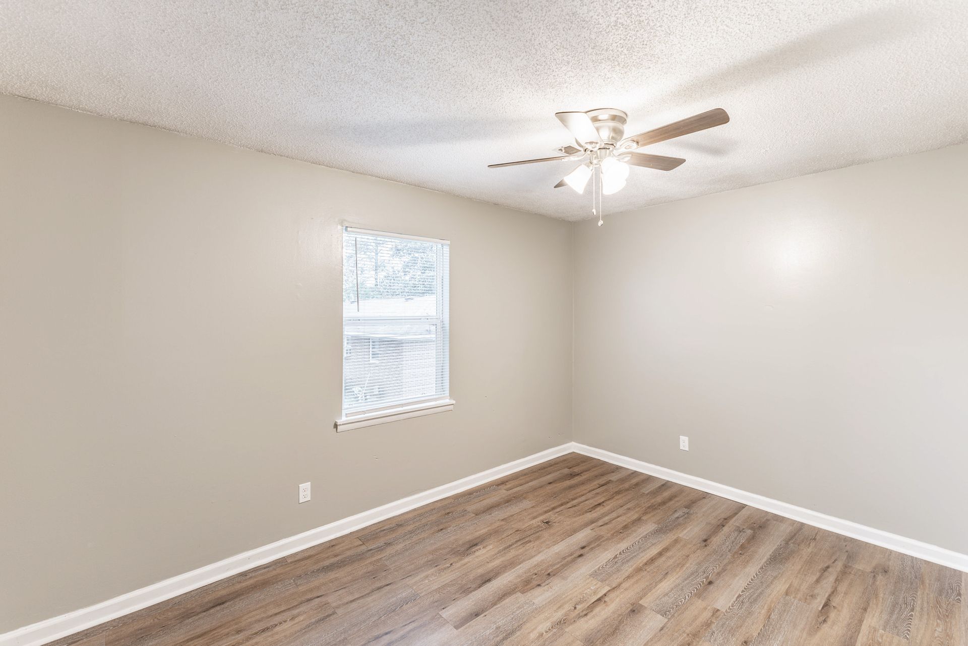 An empty room with a ceiling fan and a window.