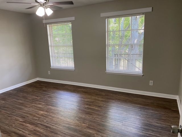 An empty bedroom with hardwood floors , two windows and a ceiling fan.