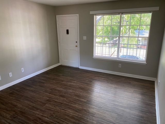 An empty living room with hardwood floors and a large window.
